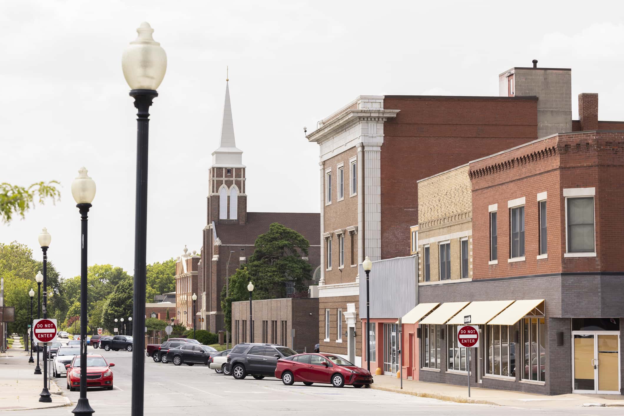 On a cloudy day, the streets of Independence, Missouri, sit quietly among the small town buildings, light poles, and street signs.